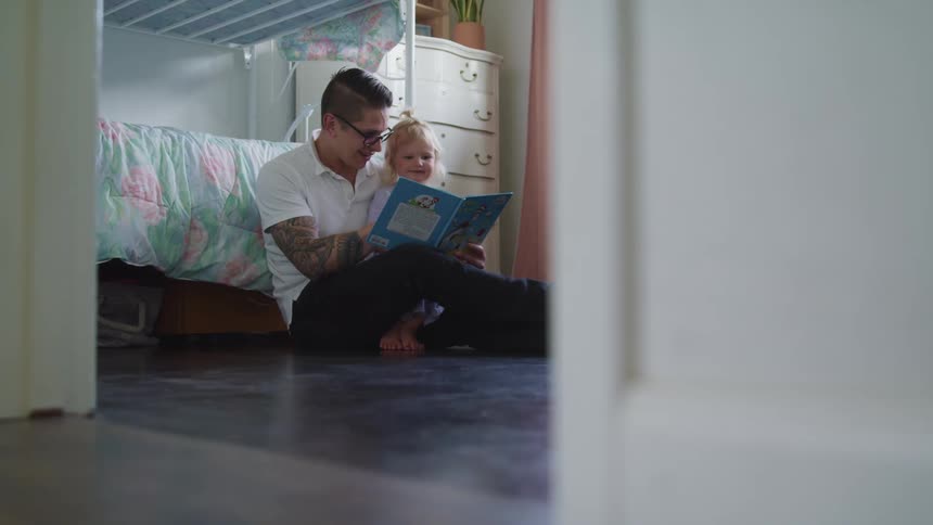 Father reads a story to her daughter while sitting in the floor of the bedroom at day