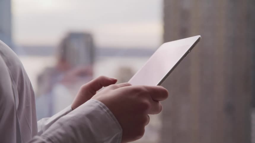 Business man in suit stands by office window and uses a tablet in the office