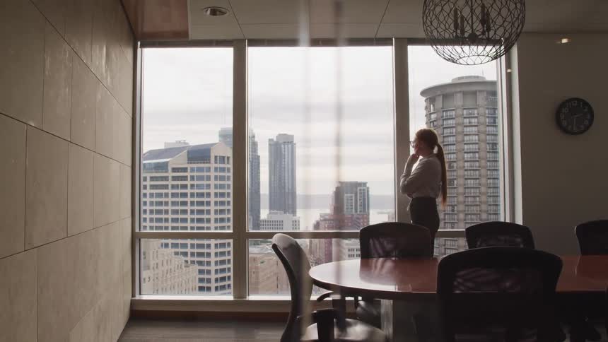 A woman standing in a office near a table and chairs with a window in the background