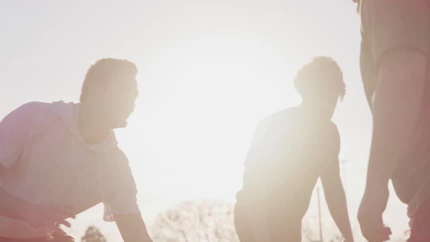 Men play football partially silhouetted by the sun overhead
