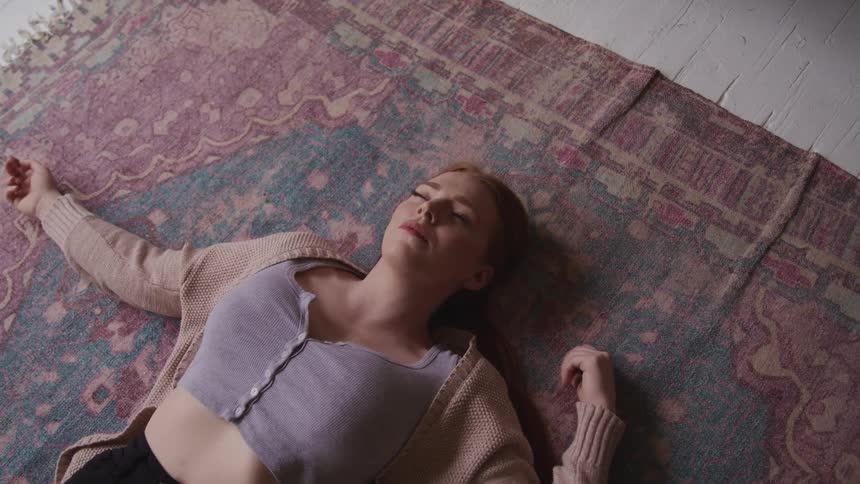Woman with red hair lies down on a carpet looking at the ceiling closes her eyes
