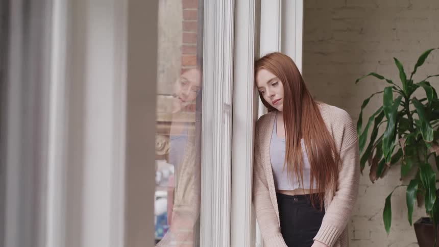 A red haired caucasian female leaning on a wall with a sad face