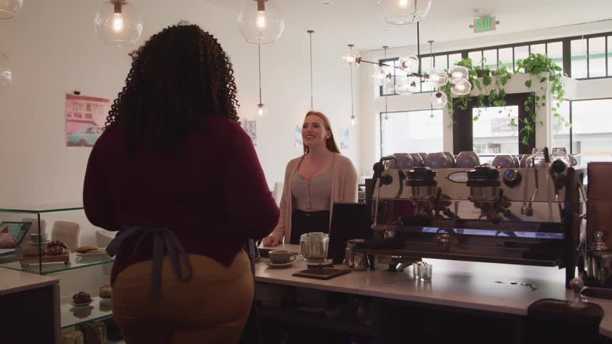 A customer stands in front of a cafe worker at the front counter