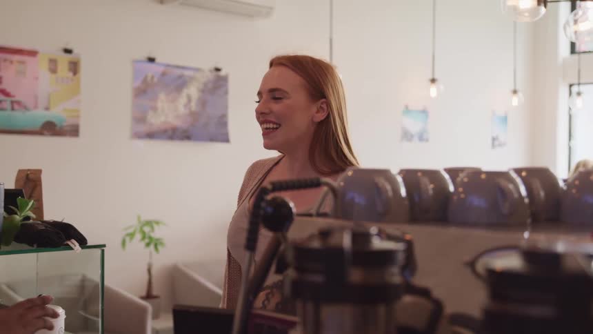 A woman standing at the counter of a cafe smiles at the employee on the other side