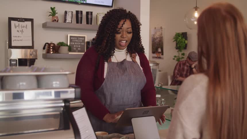 A woman with an apron behind the counter in a shop talking to another woman