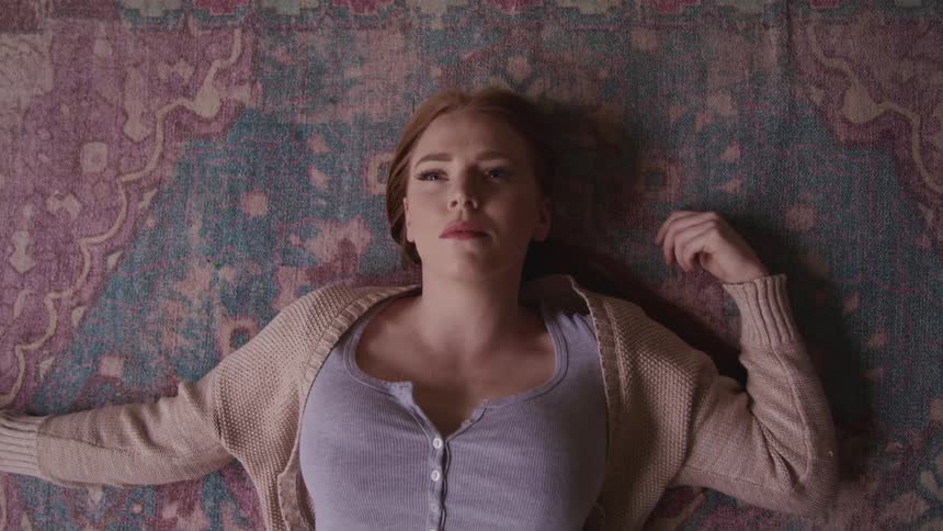 A teenager lying on the floor with her eyes shut slowly opens them