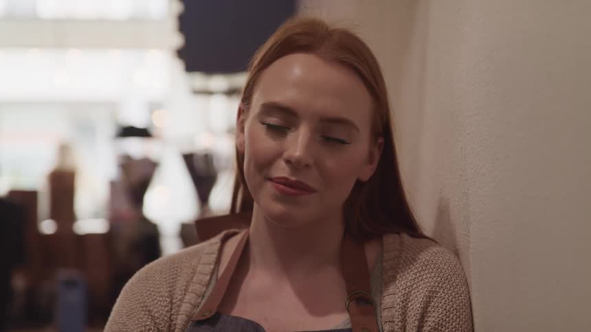 A teenage girl working in a coffee shop leans against a wall and smiles