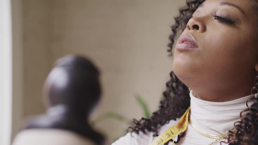 Black woman with a measuring tape around her neck moves her head around and tosses her crinkled hair
