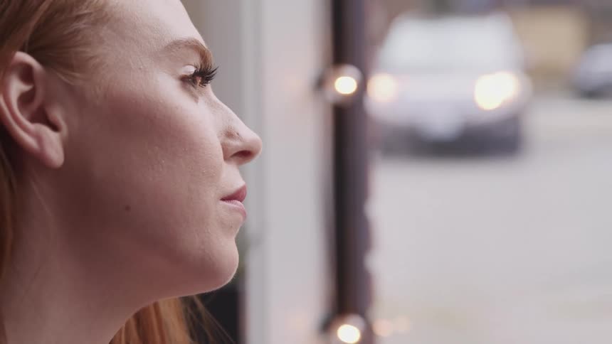 A red haired female staring out a window at moving traffic