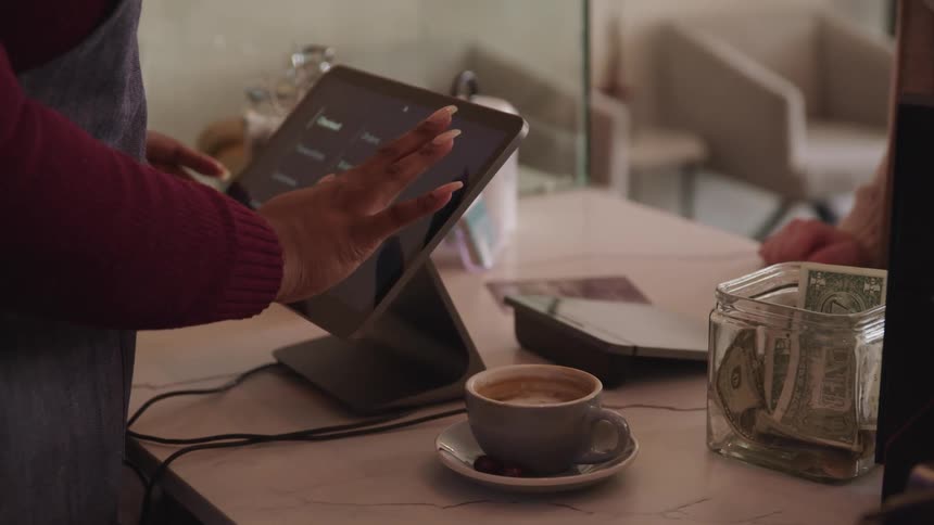 A female employee touches a tablet to ring in the order for a customer at a cafe