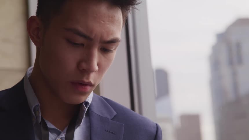 Business man looks down near window with view of downtown skyscrapers