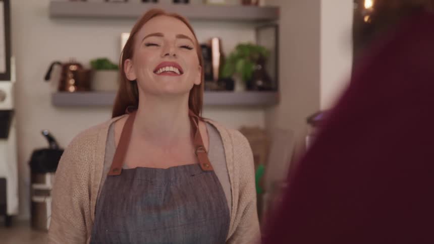 A red haired female working at a restaurant smiling and laughing with a customer
