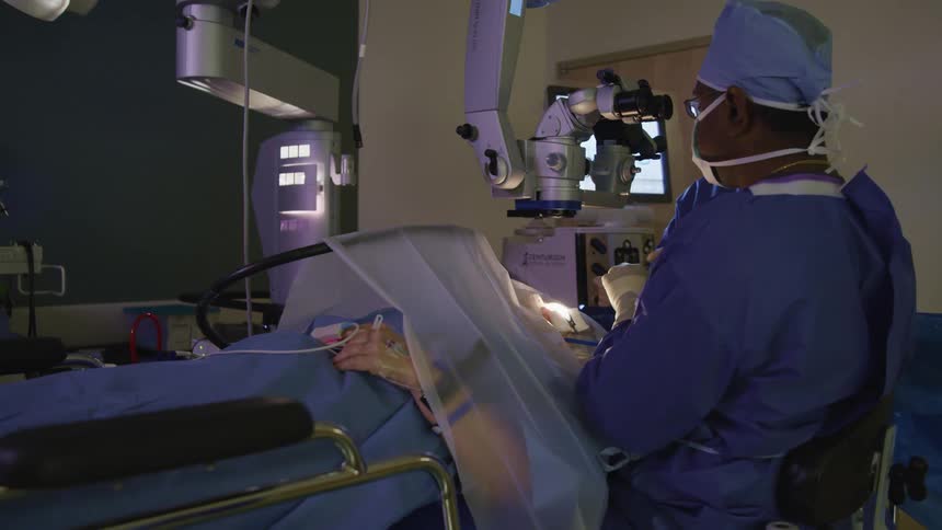 A physician performs a surgical procedure on a patient who is laying on a hospital bed