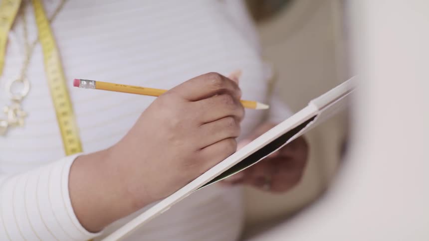A woman with a tape measure around her neck writes on a pad of paper
