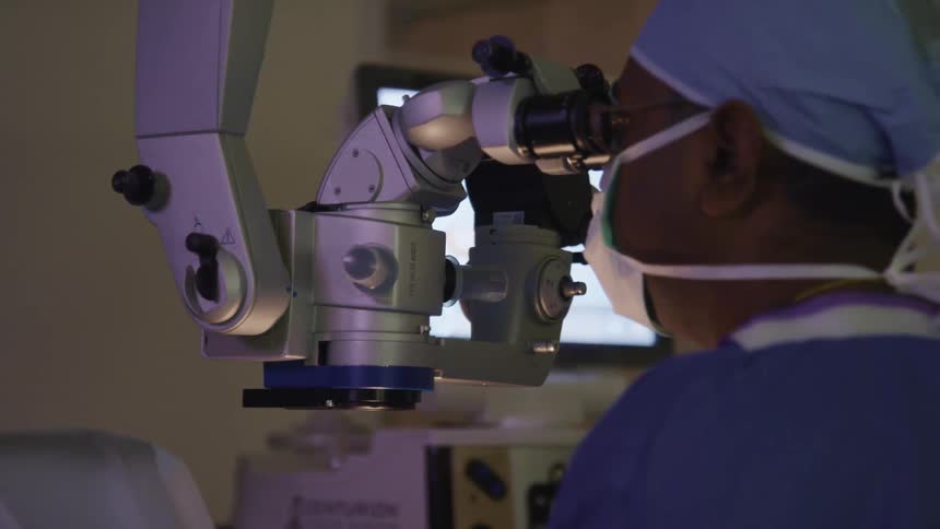 A surgeon is working on a patient with a microscope