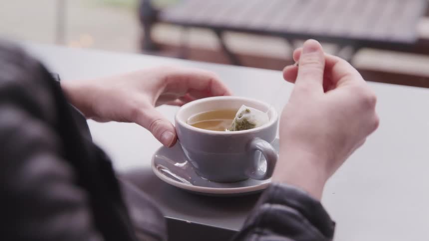 A persons hands dipping a tea bag in a teacup on a table