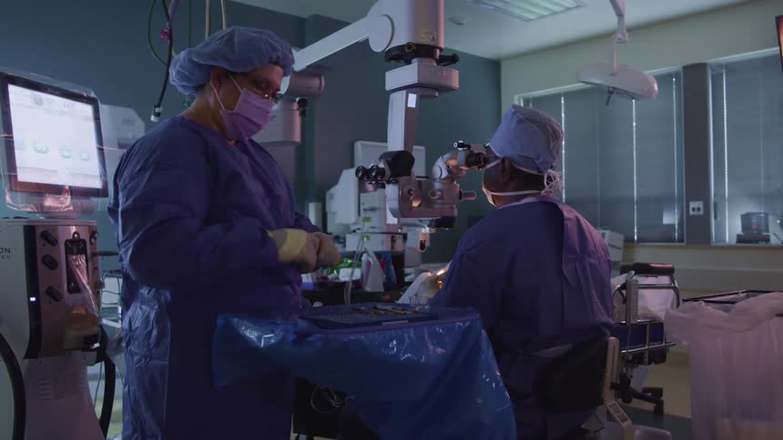 A doctor looks through a machine as a nurse stands beside him