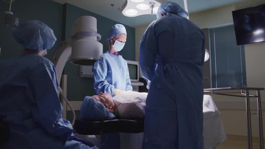 Three doctors with masks and gloves operating on a patient underneath lights
