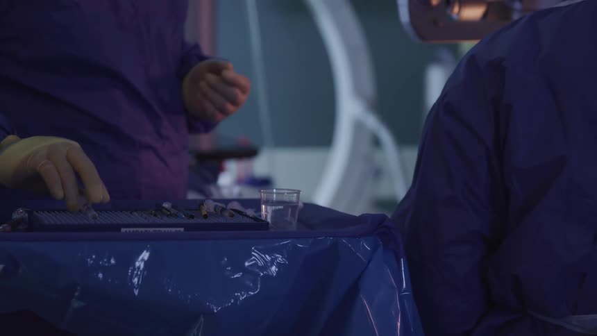 A doctor with scrubs and gloves handing a syringe to another doctor