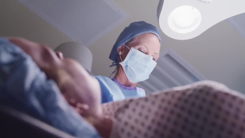 A doctor with a mask and scrubs working on a patient underneath lights