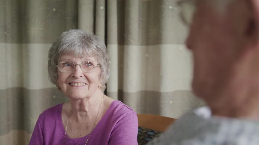 An elderly woman smiles at her husband