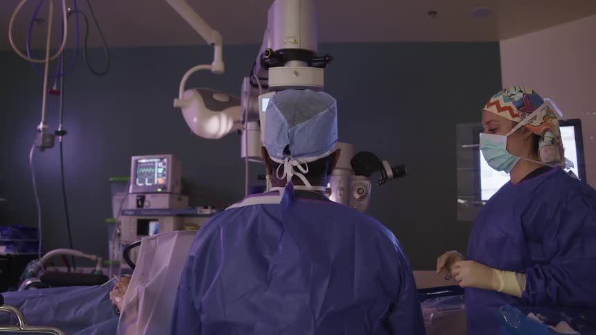 A doctor and nurse perform surgery on a patient in a hospital room
