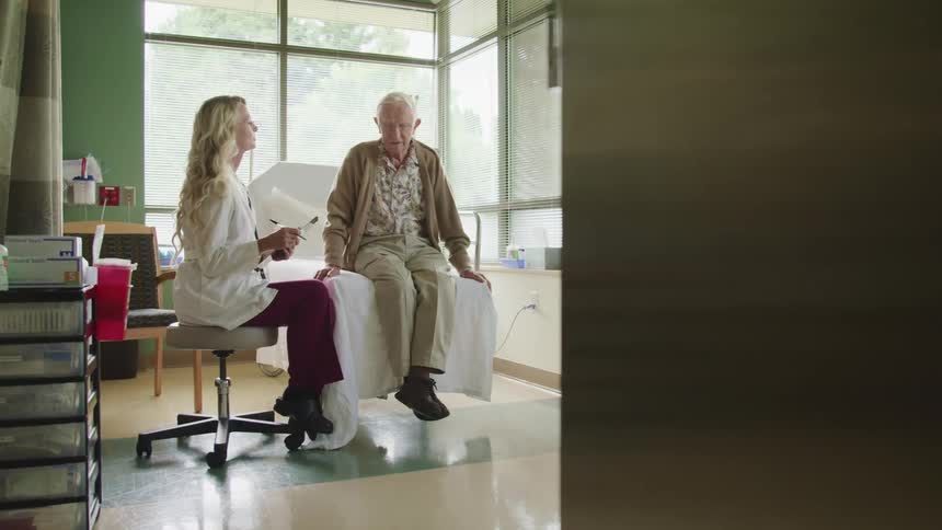 Doctor wearing lab coat explains something to an elderly patient sitting in a bed