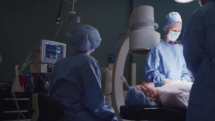 A surgical nurse monitors the vital signs of a patient as surgeons perform an operation
