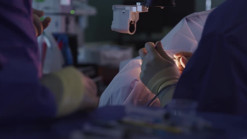 A doctor performs a procedure on a patient while a nurse hands her equipment