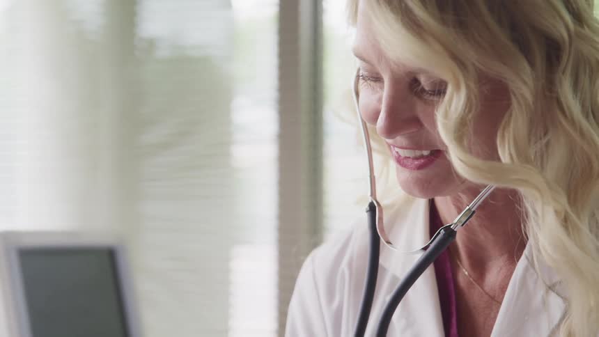 A doctor smiles while using a stethoscope in her office