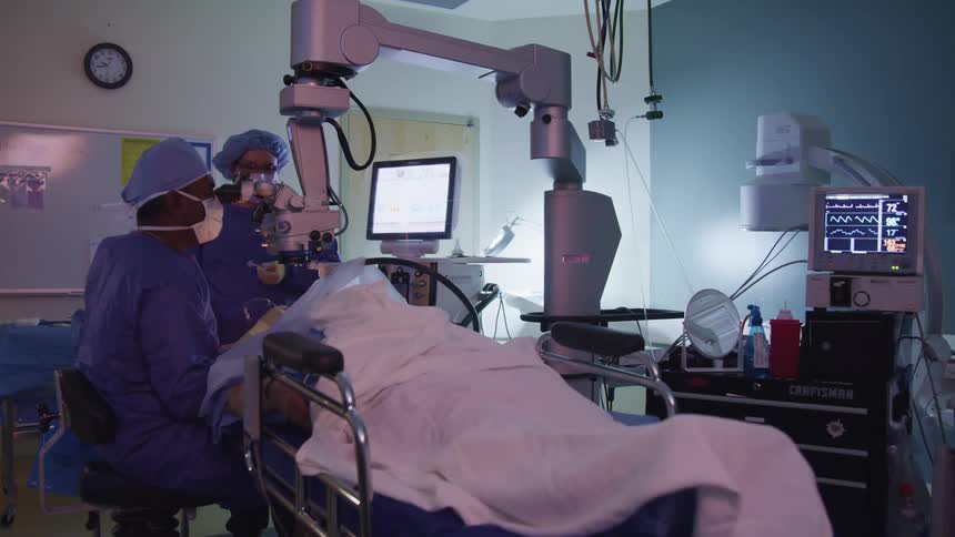 Assistant stands ready as dentist works on patient lying down