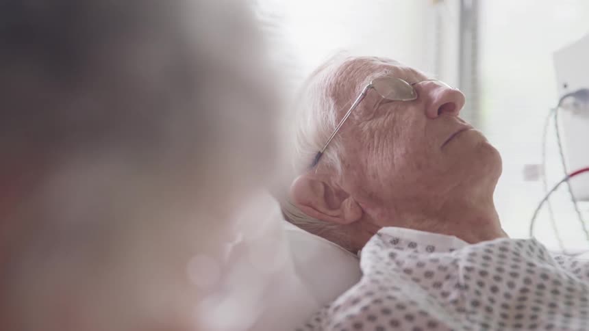 A man with glasses laying in a hospital bed with a hospital gown on