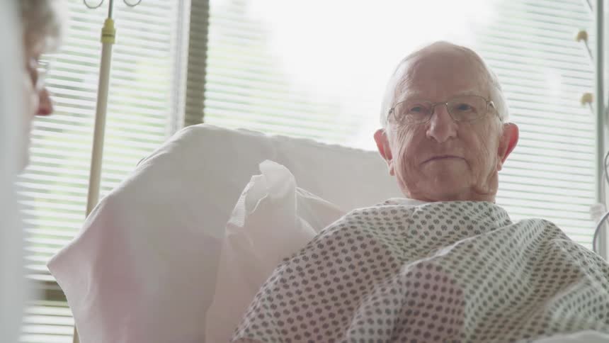 An elderly man in a hospital bed next to a visitor