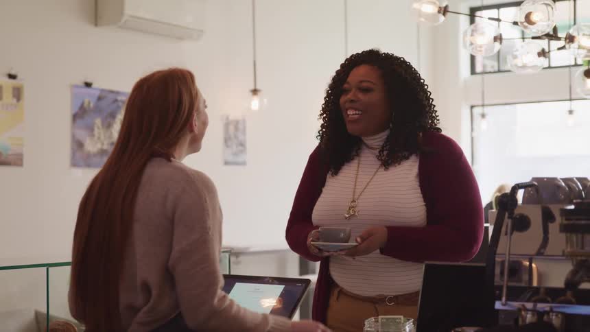 A cafe employee hands a customer a cup of coffee at the cafe counter