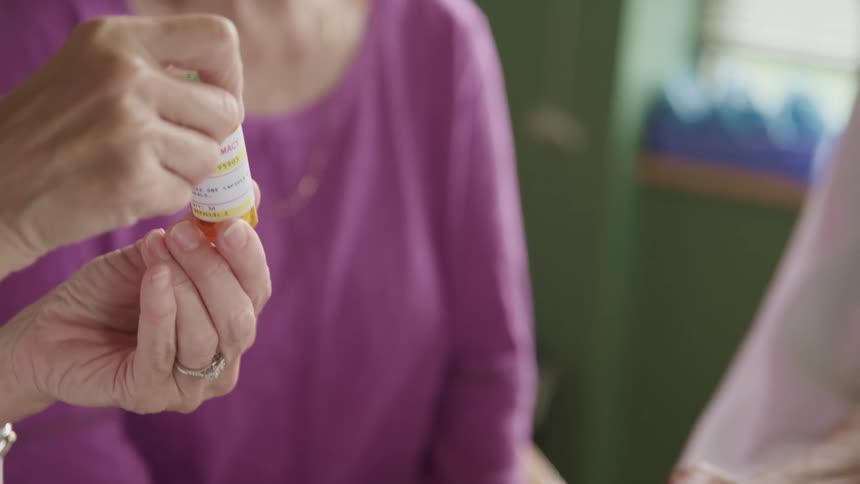A woman shows two other people a bottle of medication