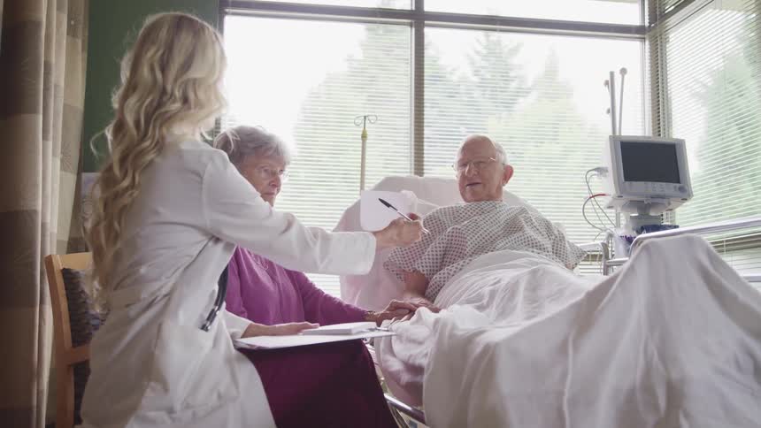 Female doctor handing her elderly patient a prescription in hospital room