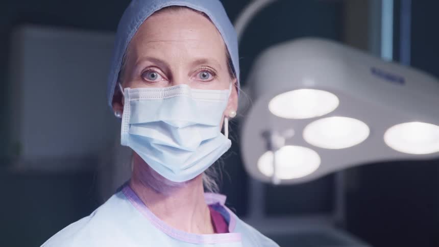 A middle aged female surgeon in personal protective equipment turns her head to look into the camera