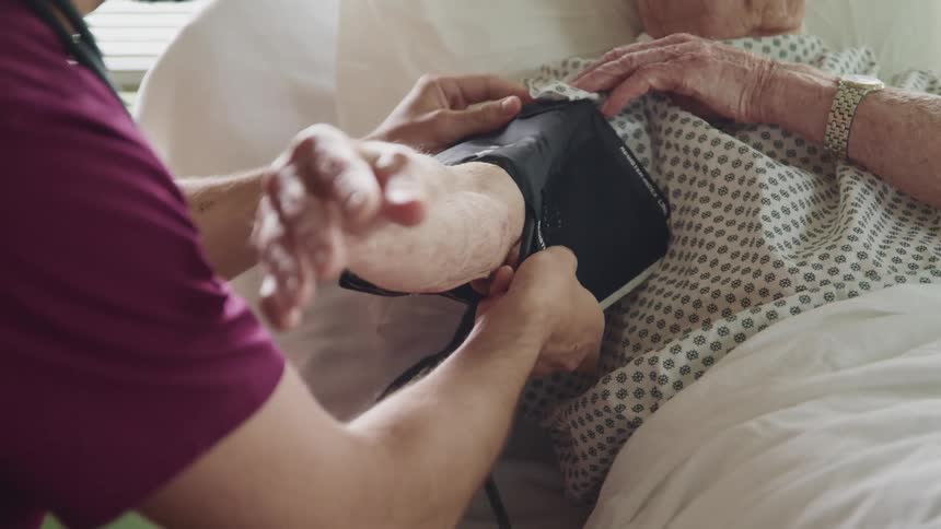 A nurse with a stethoscope and scrubs checking the blood pressure of a patient in a hospital bed