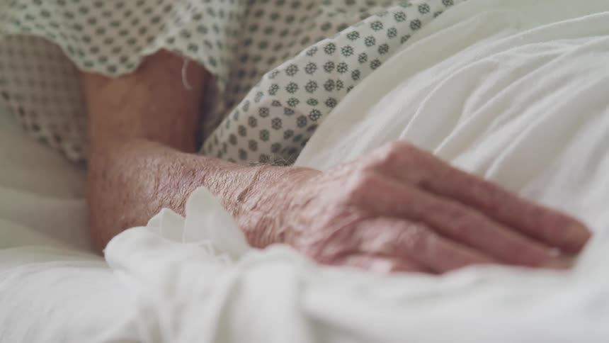 Elderly person lays in bed covered with a white sheet