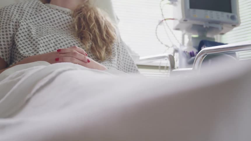 A female lays in a hospital bed beside a medical machine