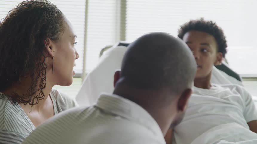 A child in a hospital bed talks with his parents who sit by his bedside