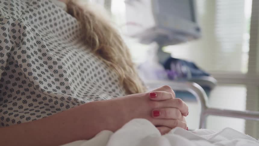 Woman holds her hands together while laying on a hospital bed
