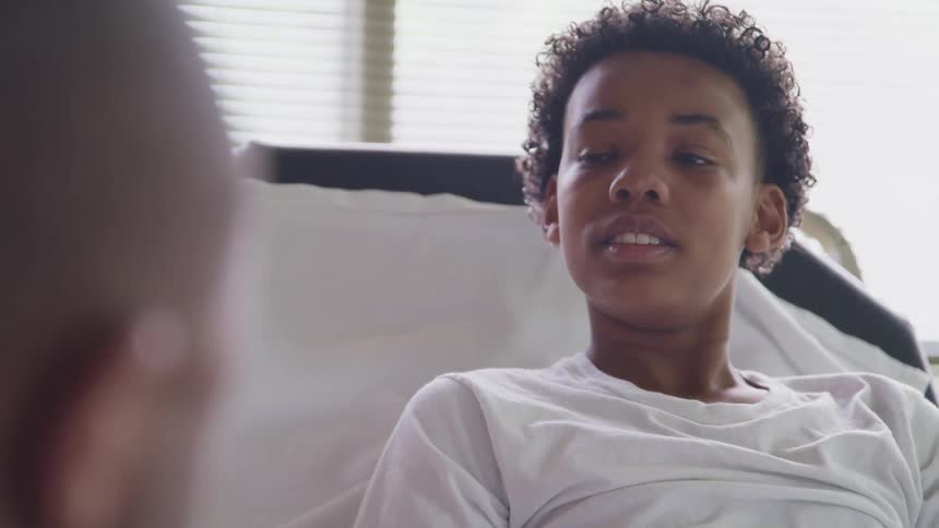 Young boy sitting in a hospital bed talks to an adult