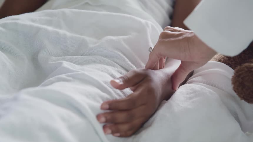 A doctor checking the pulse of a patient on a bed next to a stuffed toy