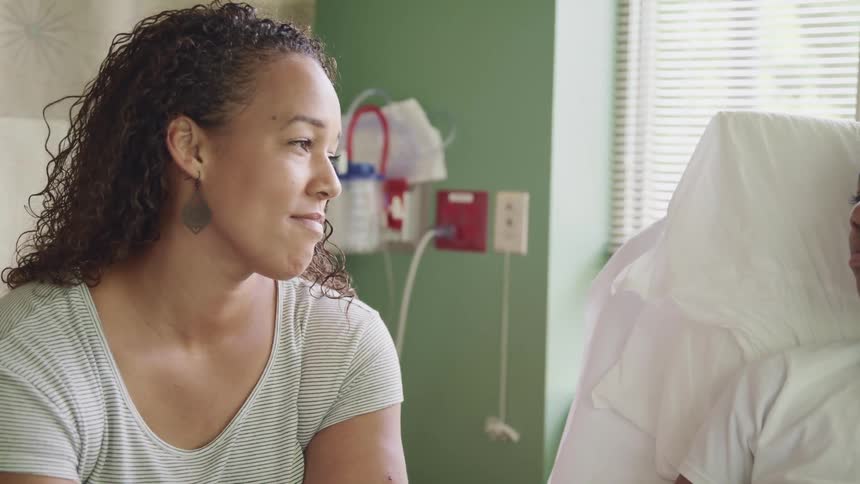 Mother looks at son laying on a bed in a hospital