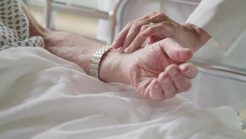 Doctor takes pulse of elderly patient lying in bed