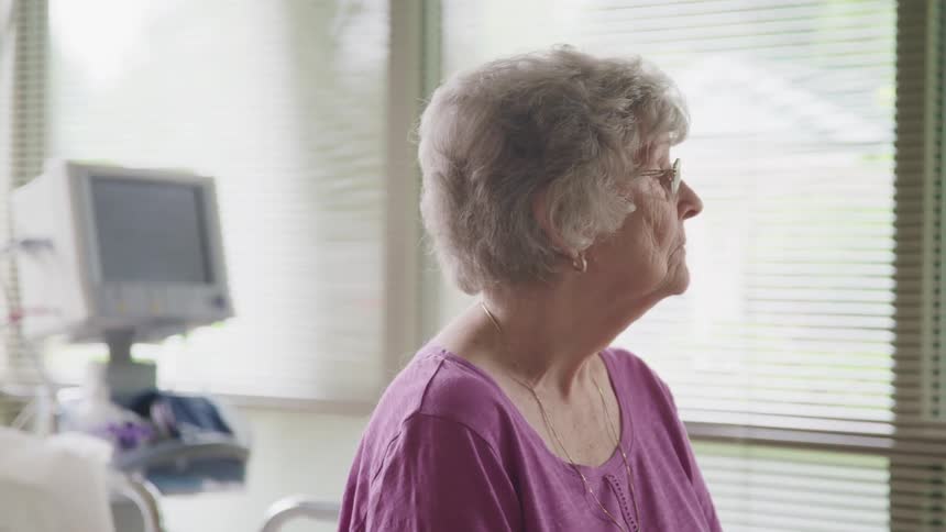 Elderly woman sitting in a hospital bed looks out the window pensively