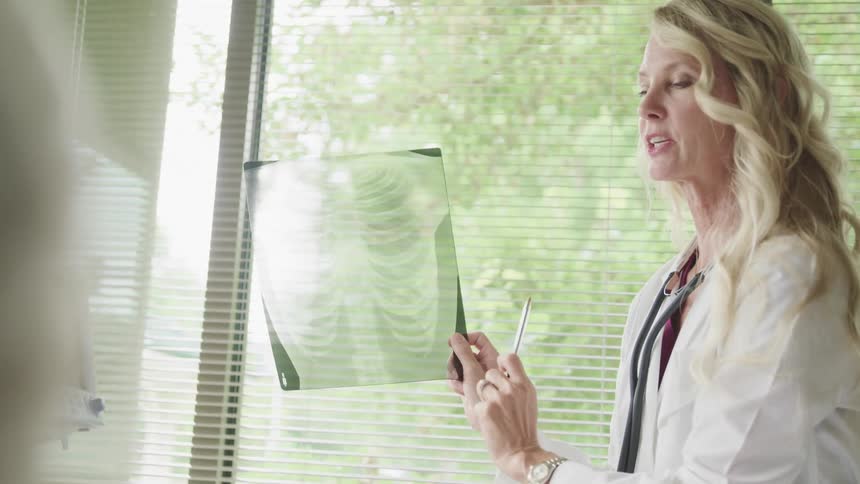 A female physician holds an xray of a rib cage up while discussing the results with a patient