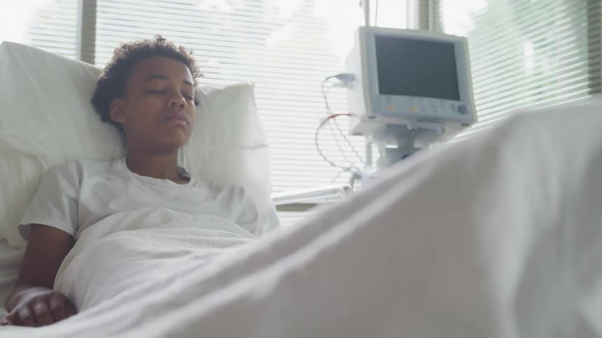 Patient lays propped up on pillows in hospital bed with eyes shut