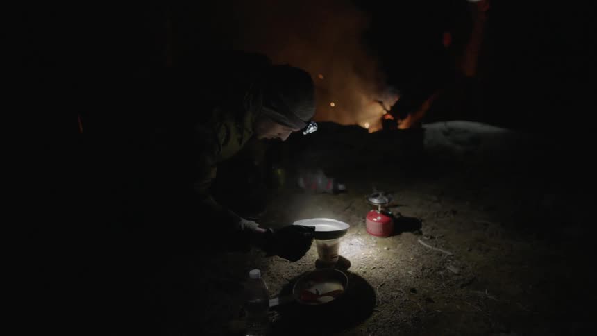 A man pours hot water while sitting next to a campfire